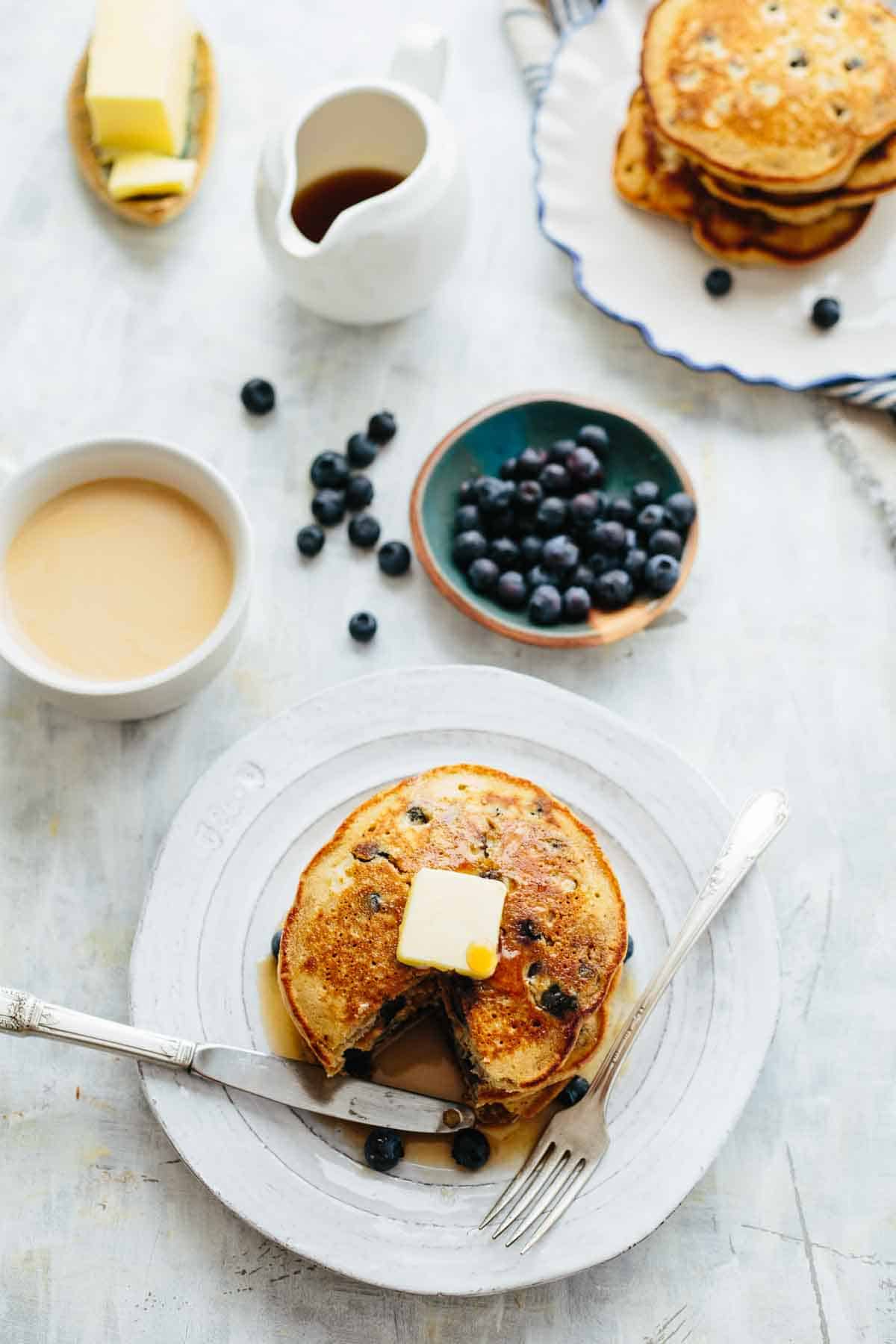 A breakfast table scape with pancakes, berries, coffee, butter and syrup.