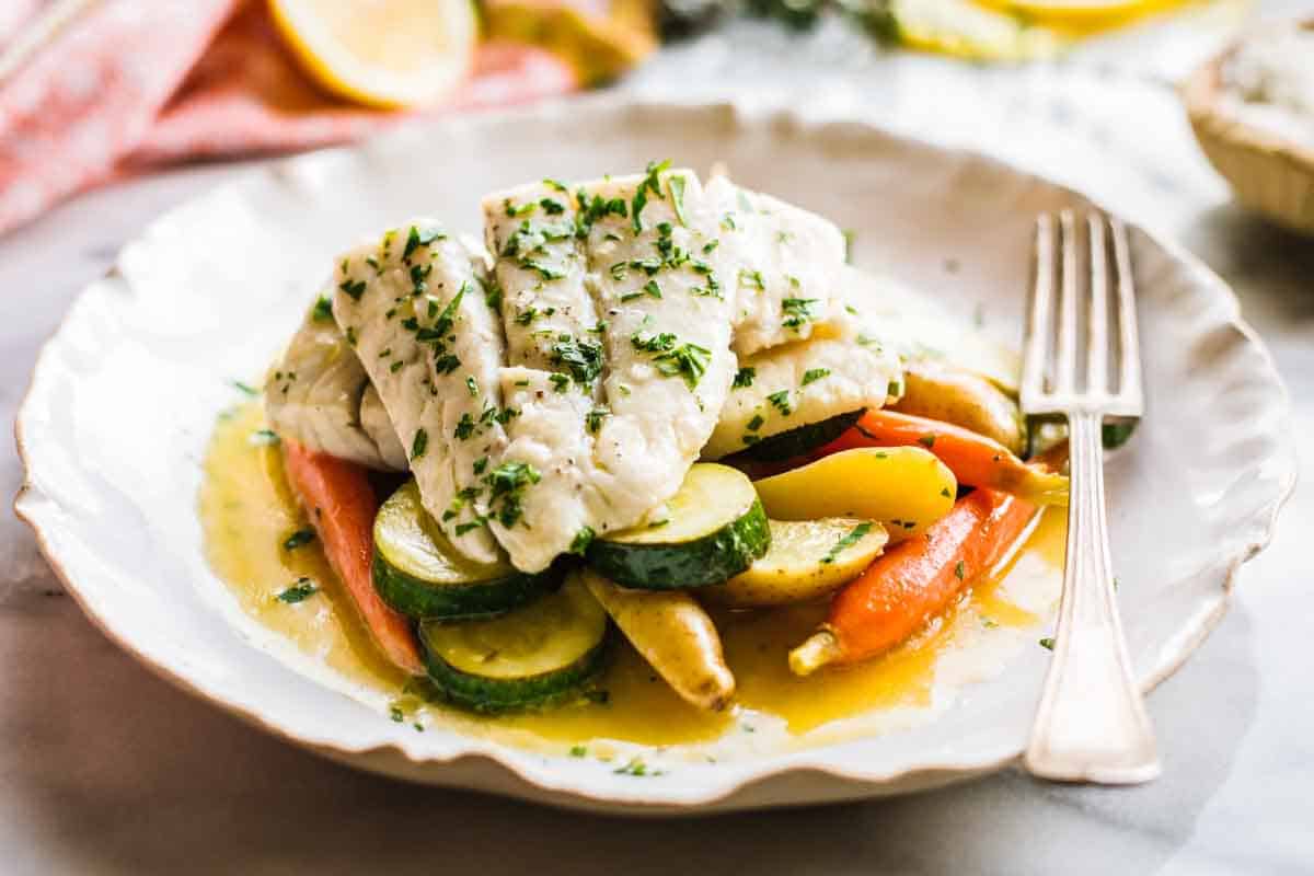 Poached barramundi on a plate with vegetables in a butter sauce.
