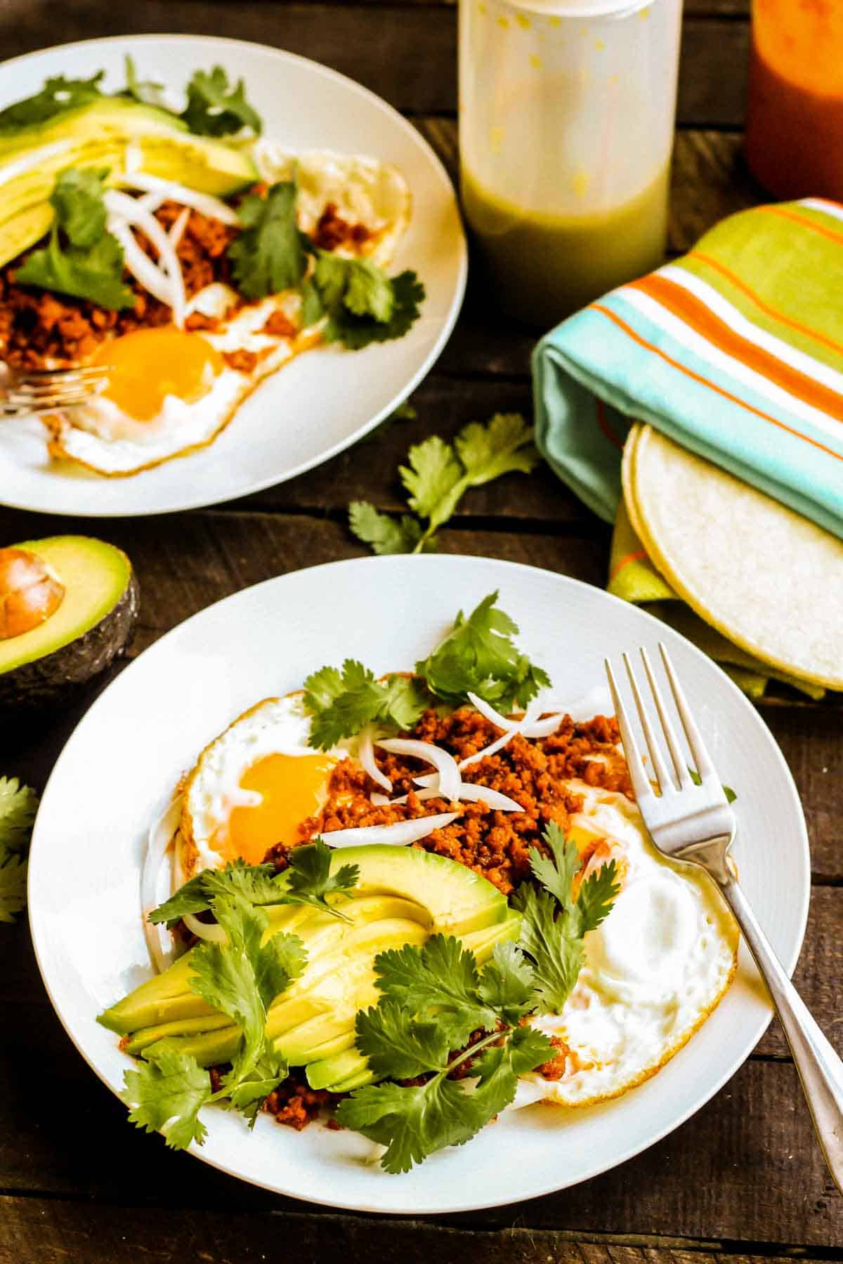 Chorizo with eggs and avocado on a plate with a fork and warm tortillas wrapped in a towel.