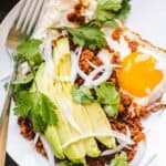 A white plate with fried eggs, chorizo and avocado on top with a fork.