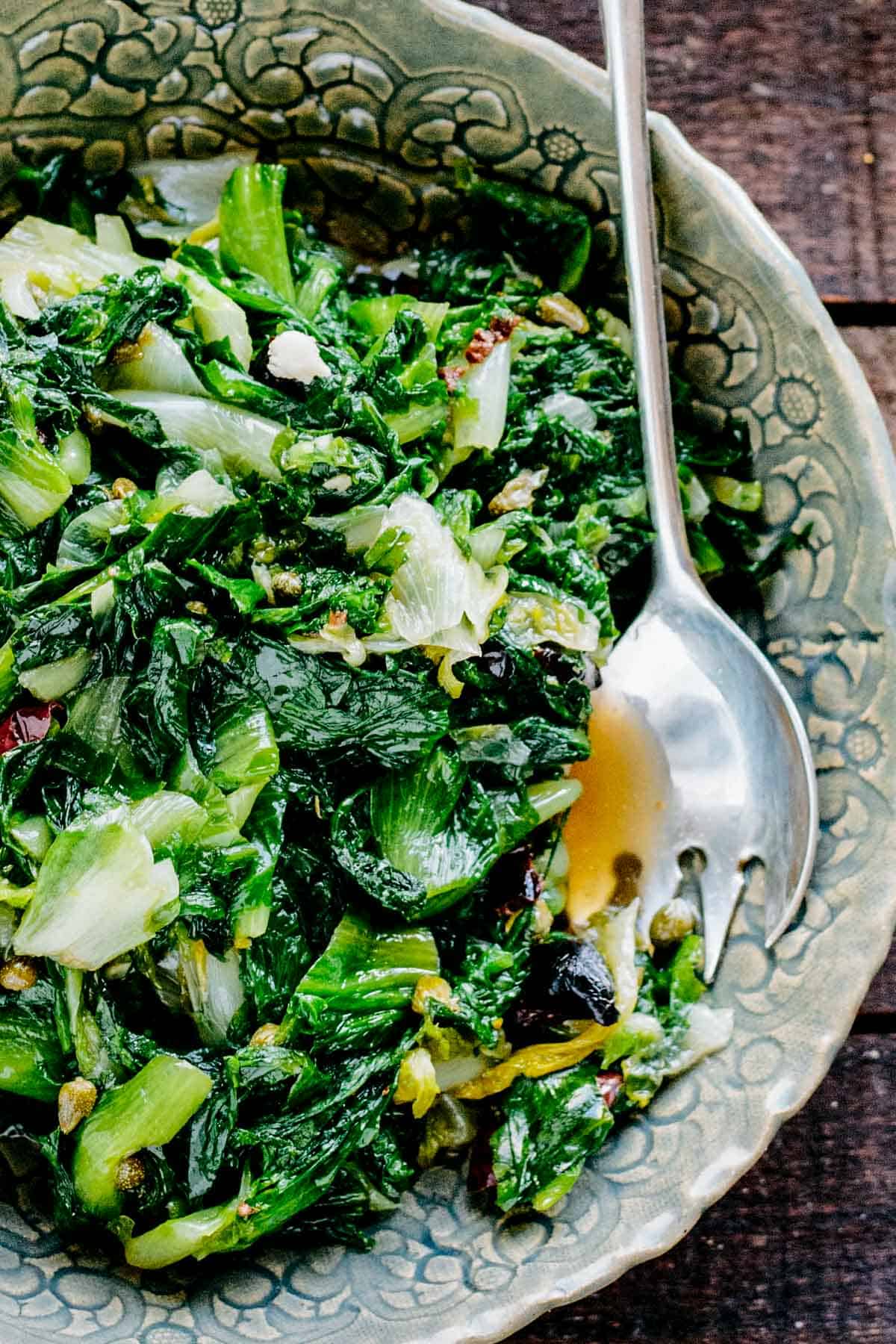 Leafy green pieces of sautéed escarole with capers and olives.