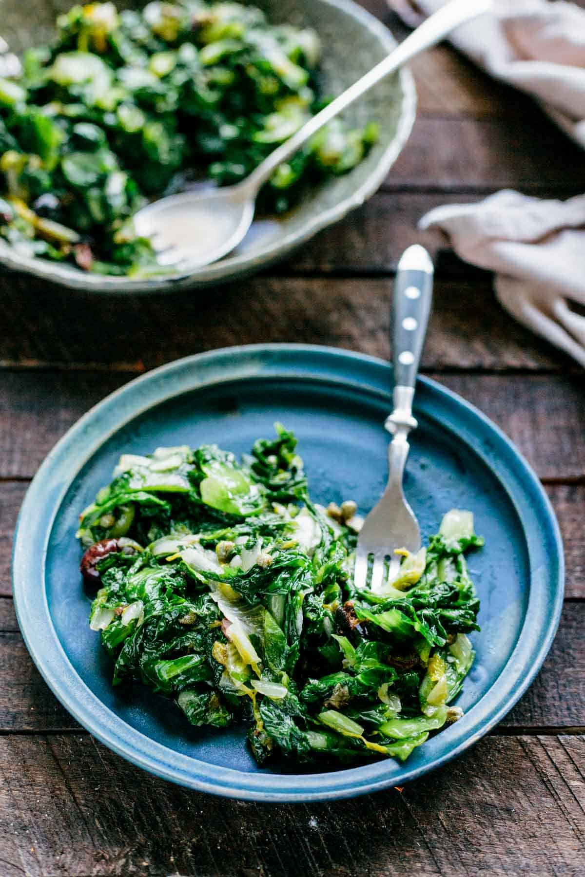 A blue plate of sautéed greens with a fork.