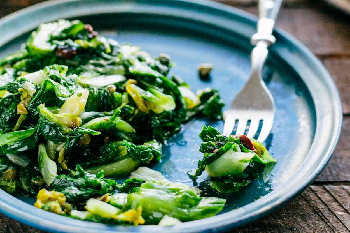 A fork scooping up sautéed Italian escarole with garlic and olives.