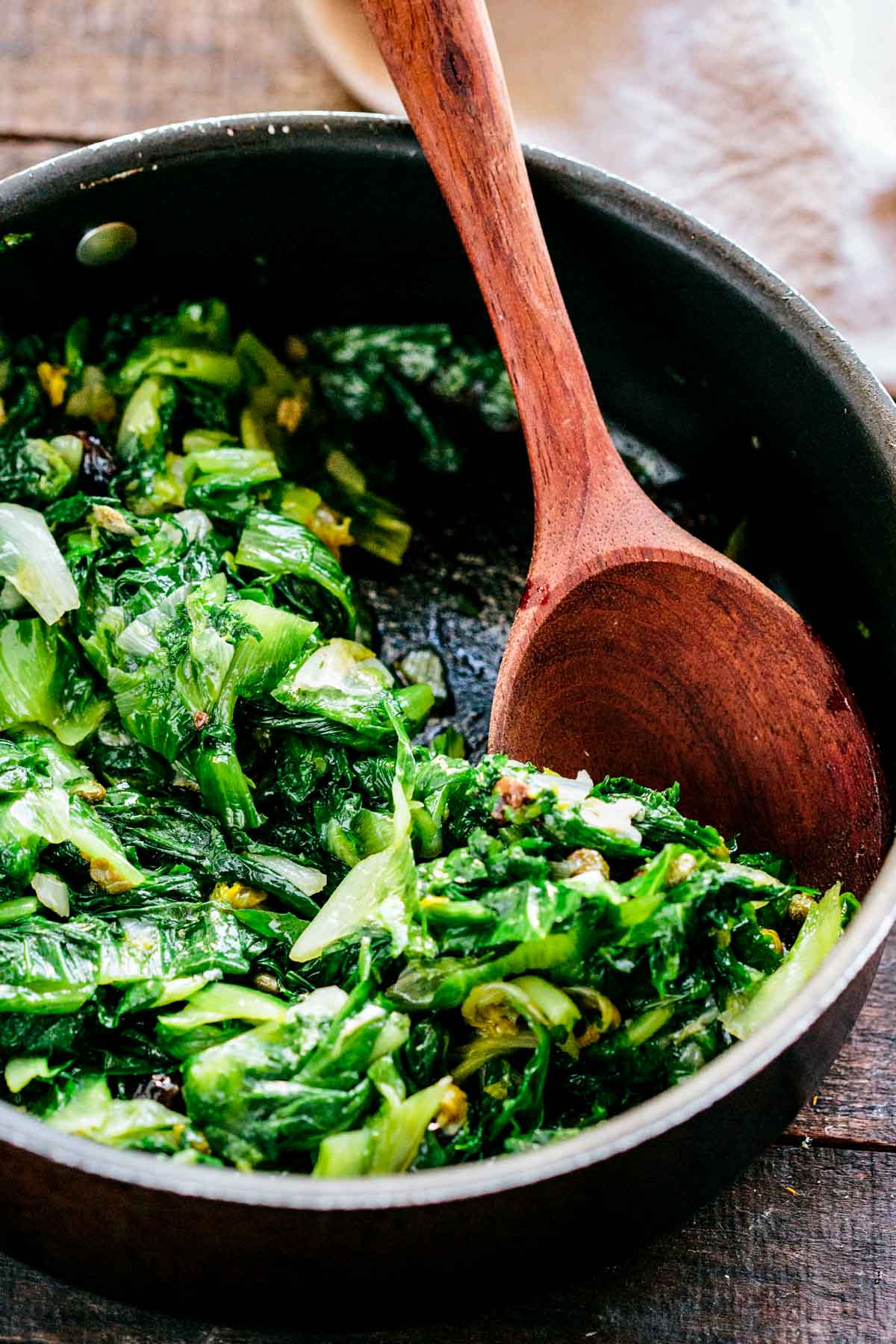 A pan and wooden spoon with Italian style sautéed escarole.