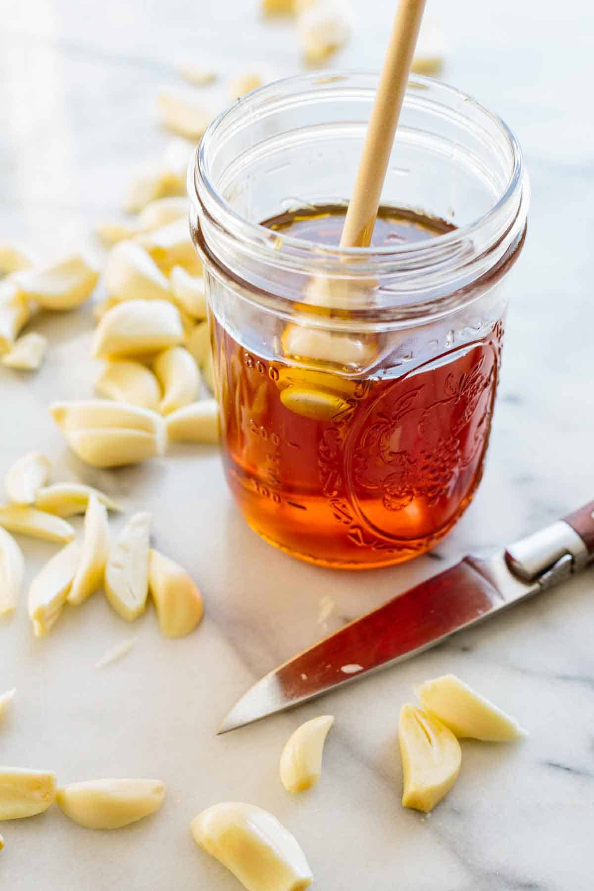 A jar of honey, cloves of garlic and a paring knife.