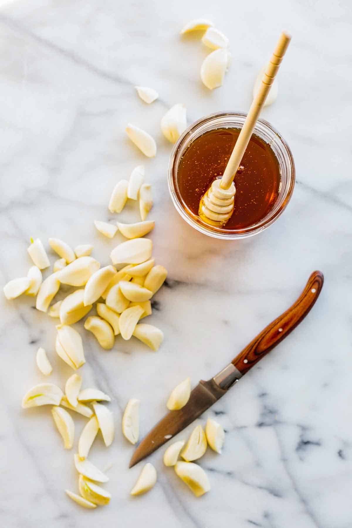 Cloves of garlic with a paring knife and a jar of honey with a honeycomb.