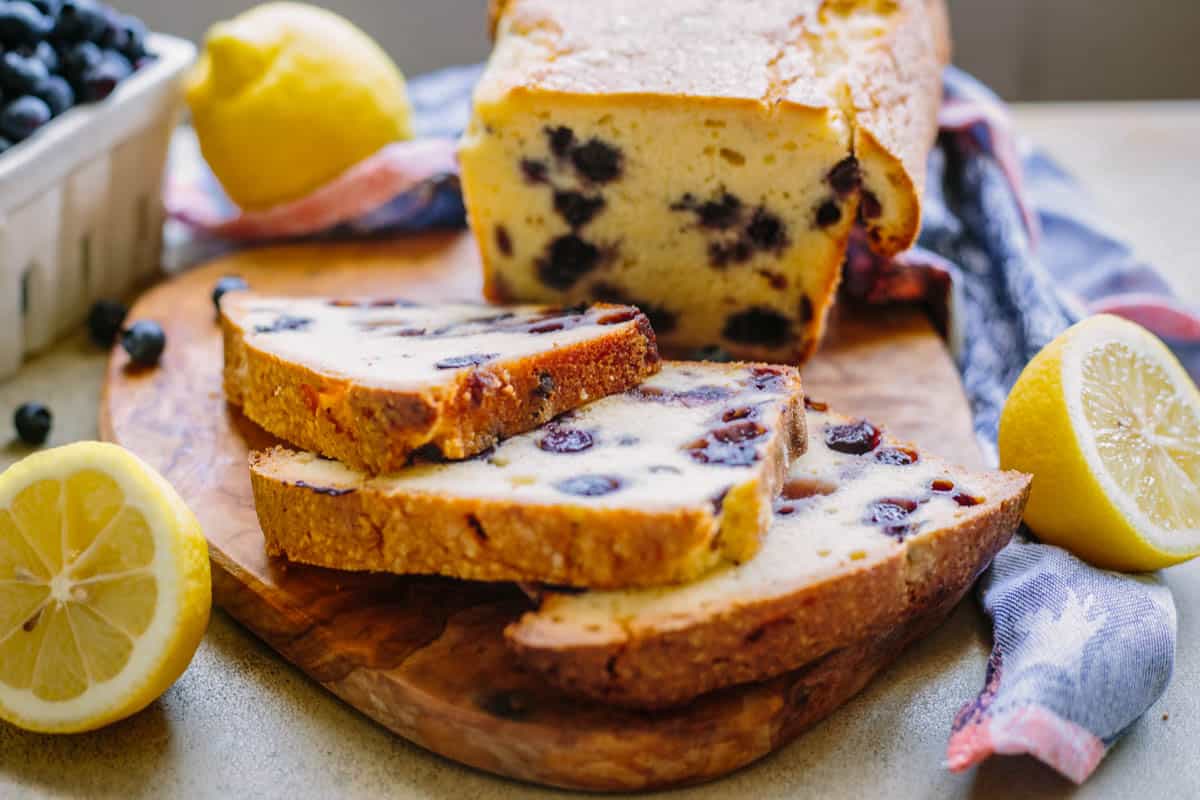 Three slices of lemon blueberry pound cake cut off a loaf on a wood cutting board.