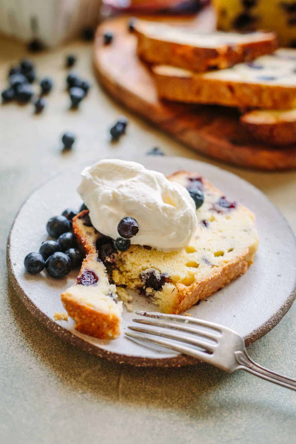 A fork cutting a bite off a slice of lemon blueberry pound cake on a small plate.