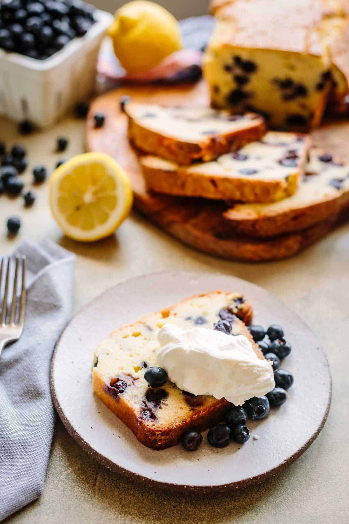 Slice of blueberry lemon pound cake with fresh blueberries and whipped cream on a dessert plate.
