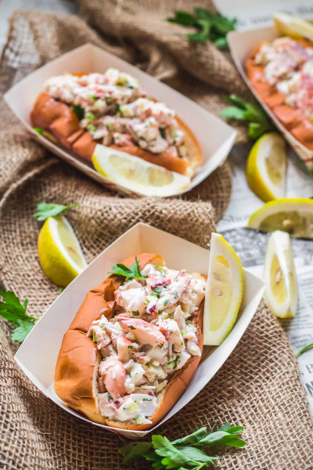 Paper plates with Maine lobster rolls and lemon wedges on newspaper. 