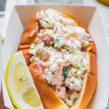 Maine lobster roll in a paper boat with a lemon wedge.