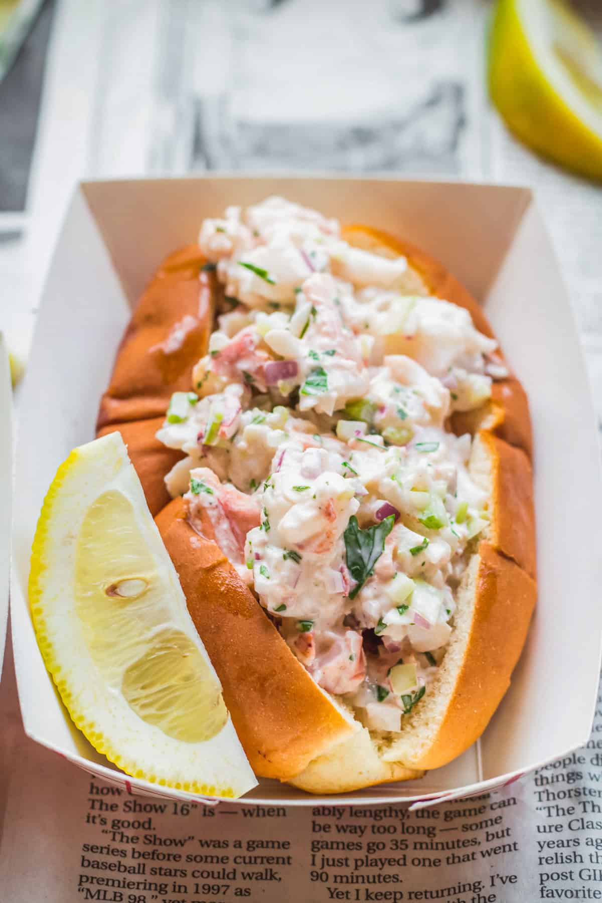 Maine lobster roll in a paper boat with a lemon wedge.