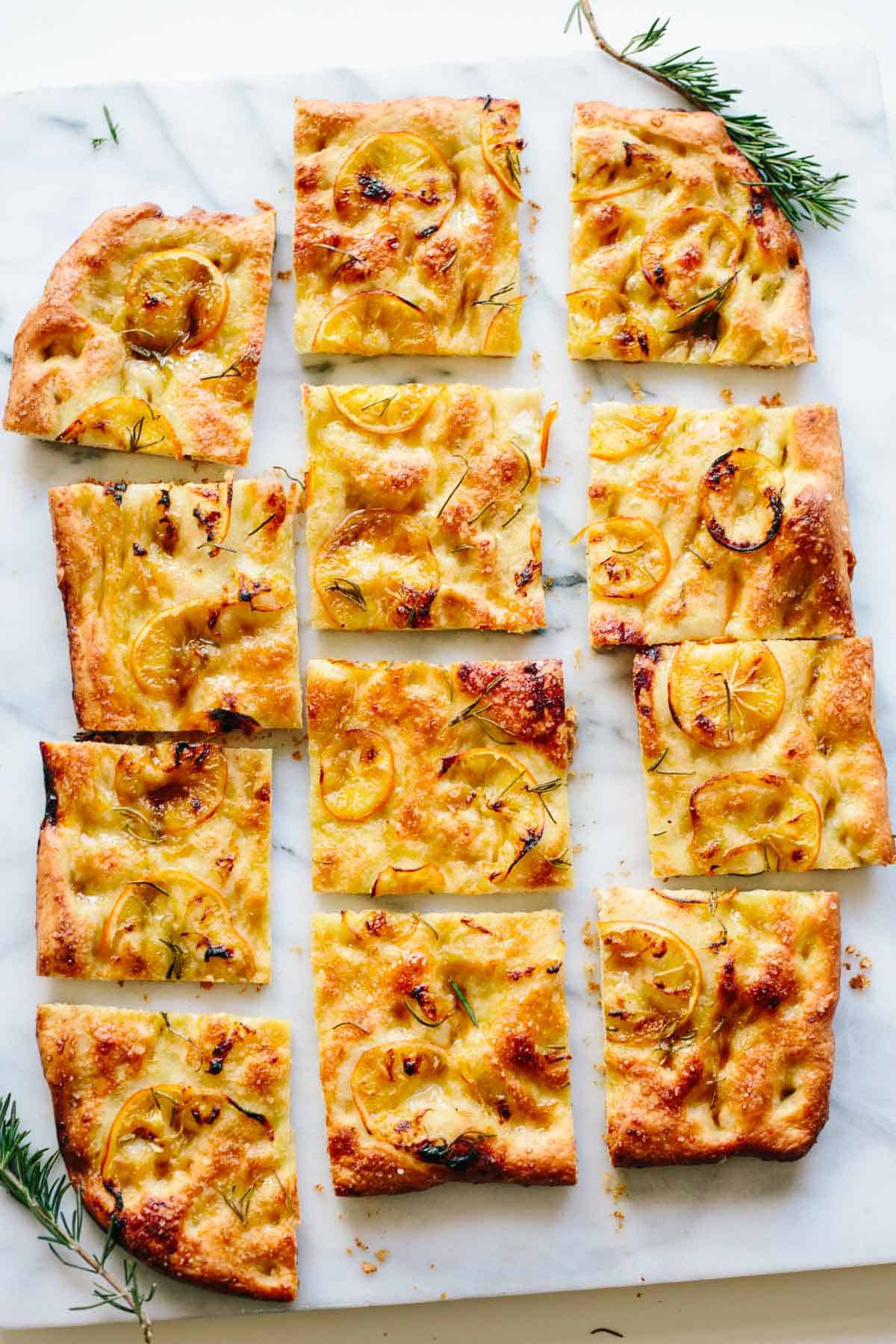 A whole focaccia cut into pieces with thinly sliced lemon and rosemary ont op.