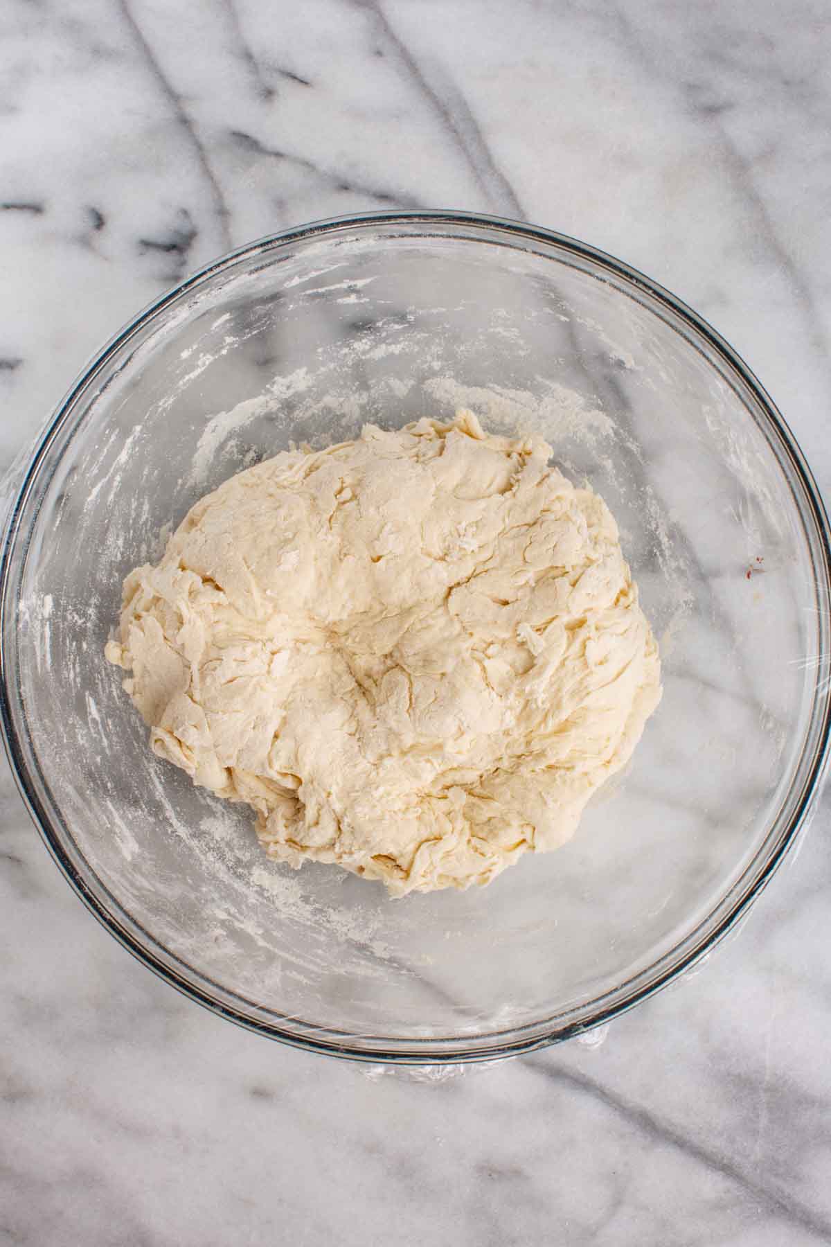 A bowl of shaggy focaccia dough being mixed.
