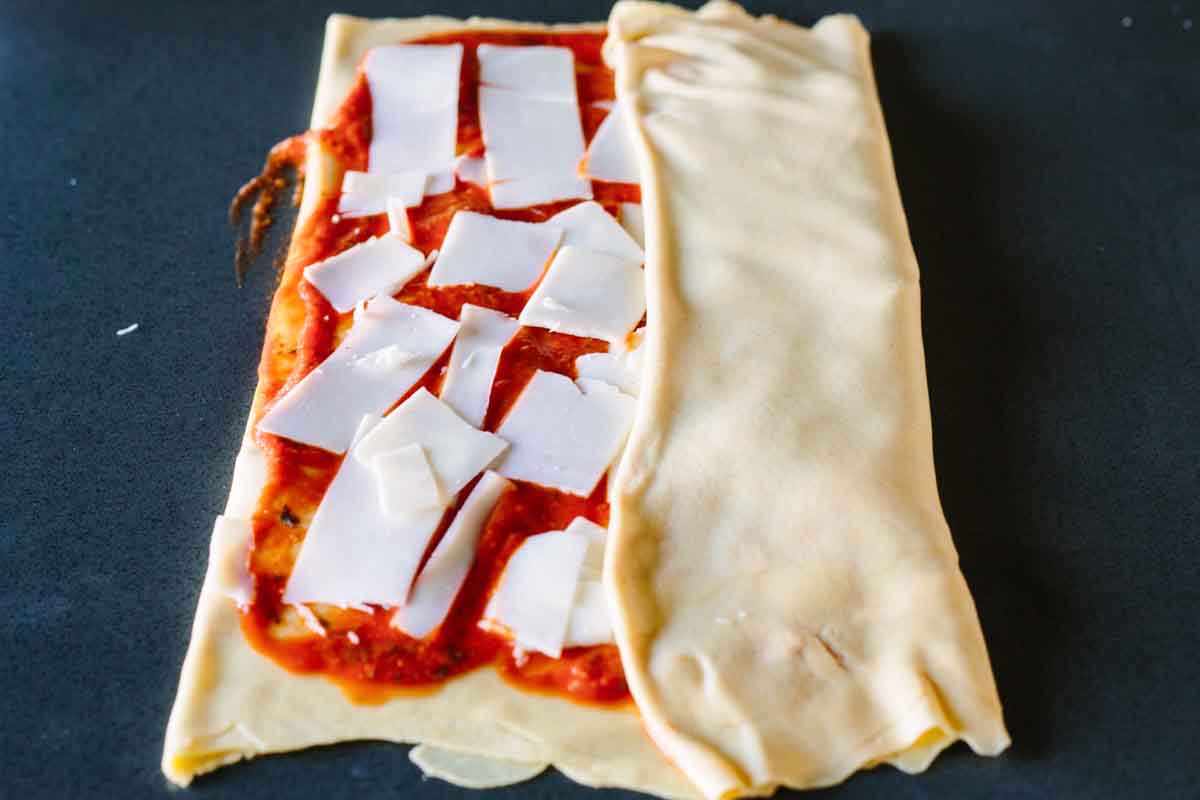 Dough being folded over tomato sauce and cheese.