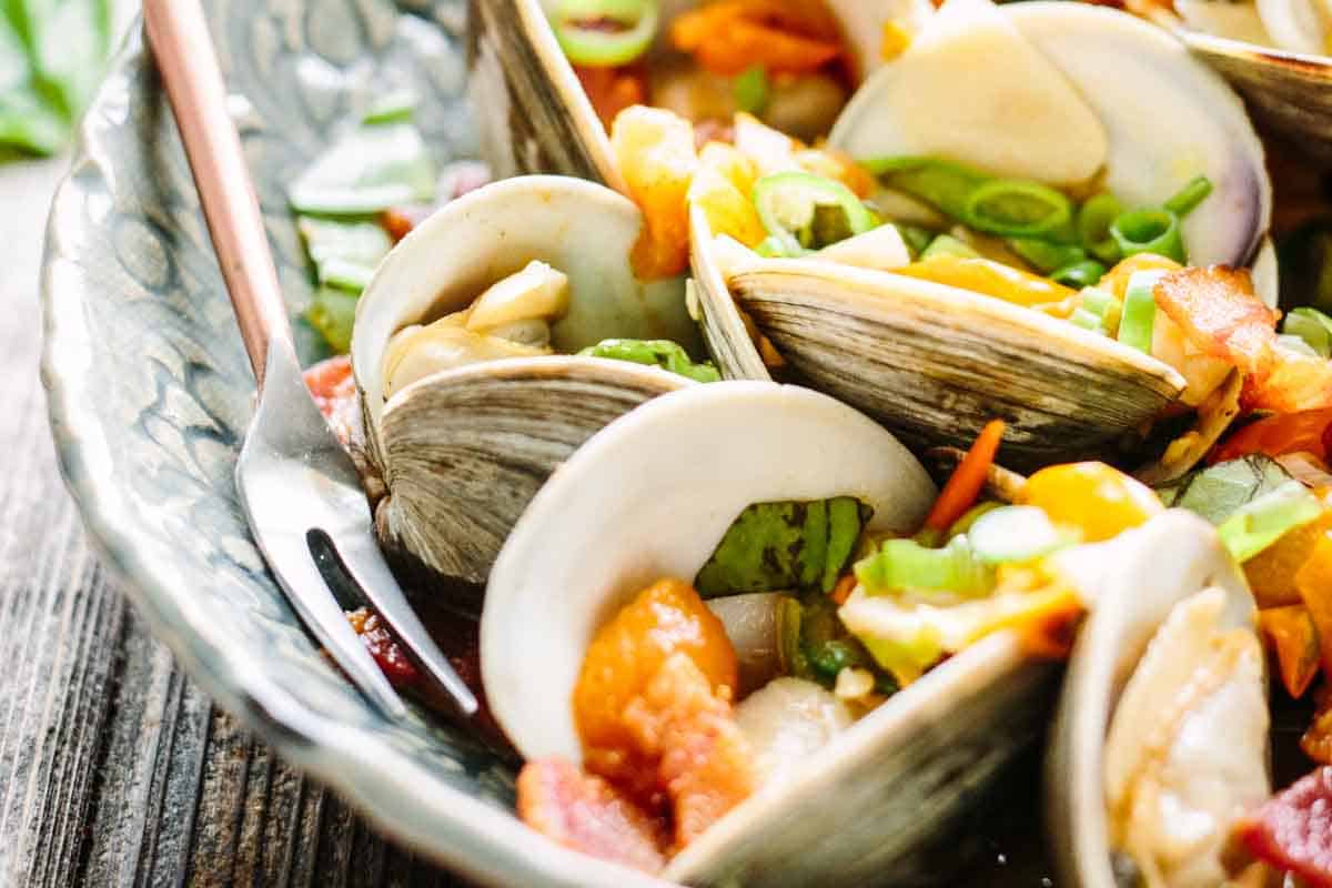 Steamed clams with herbs and tomatoes with a cocktail fork.