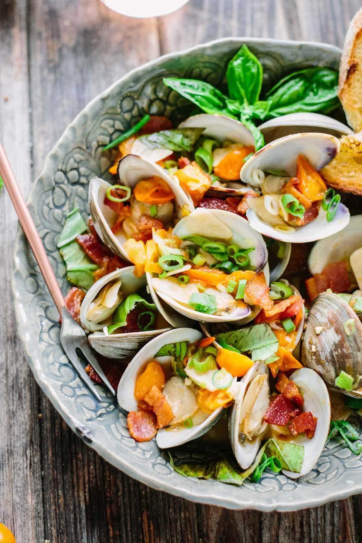 A bowl of steamed clams with bacon and tomatoes.