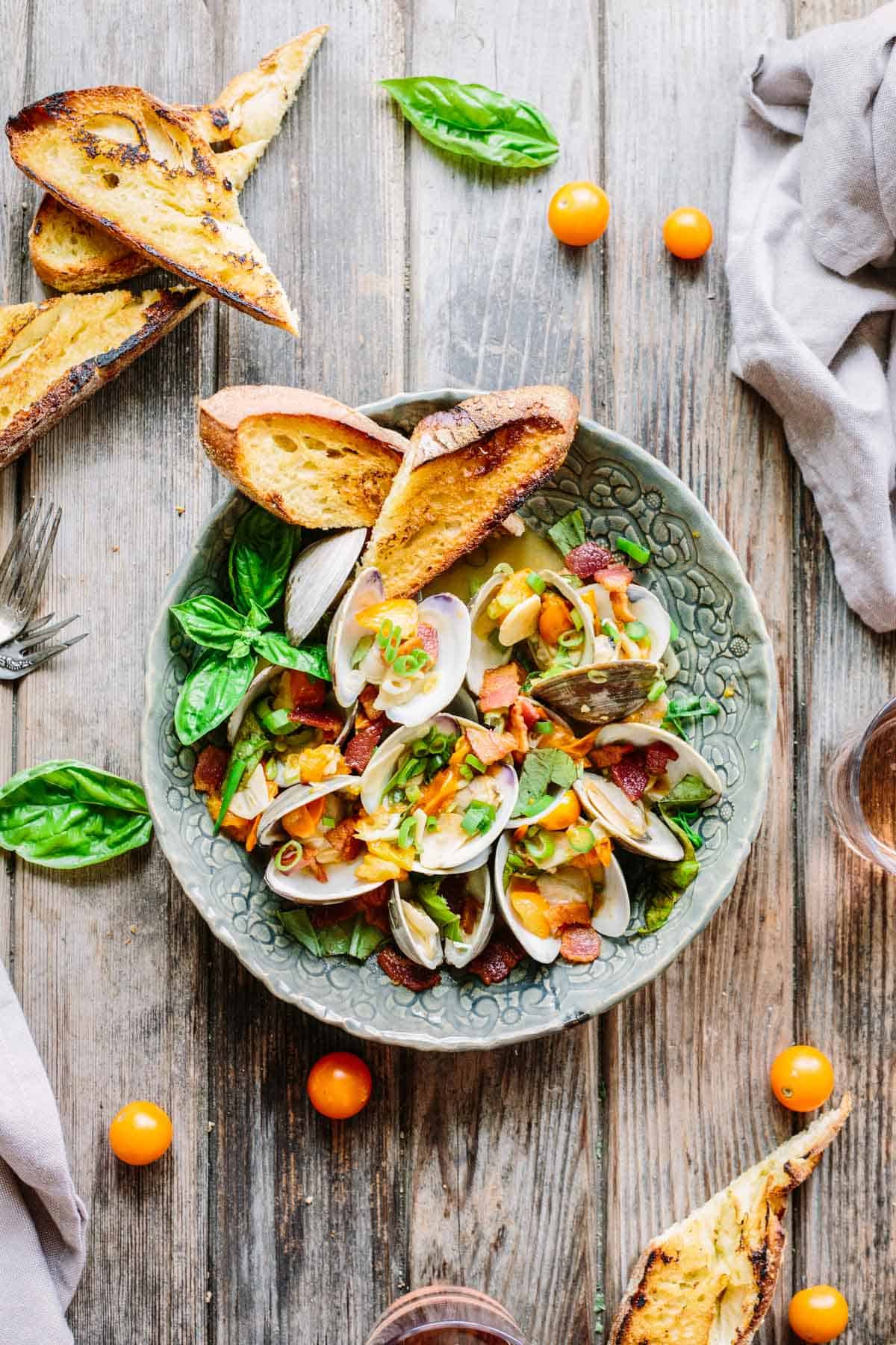 A bowl of steamed clams with bacon and tomatoes with toast.