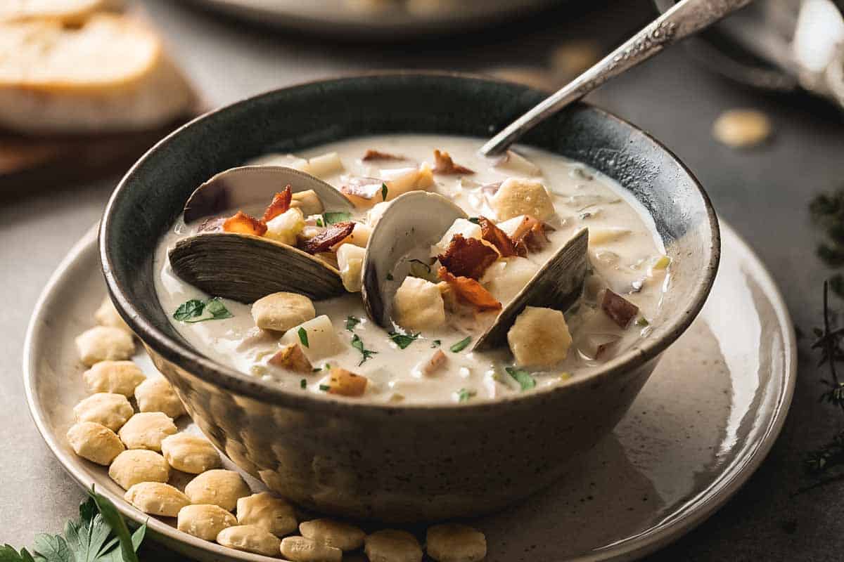 A bowl of clam chowder with a spoon and oyster crackers.