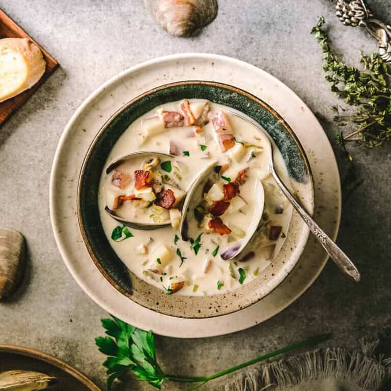A bowl of clam chowder with bread and fresh clams.