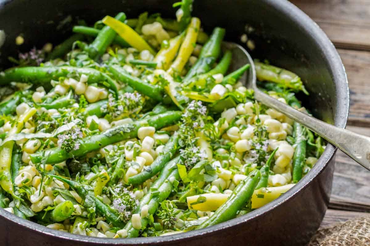 A pan filled with green beans and corn with flowering herbs.