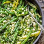 Green beans and corn in a pan with fresh herbs and a serving spoon.