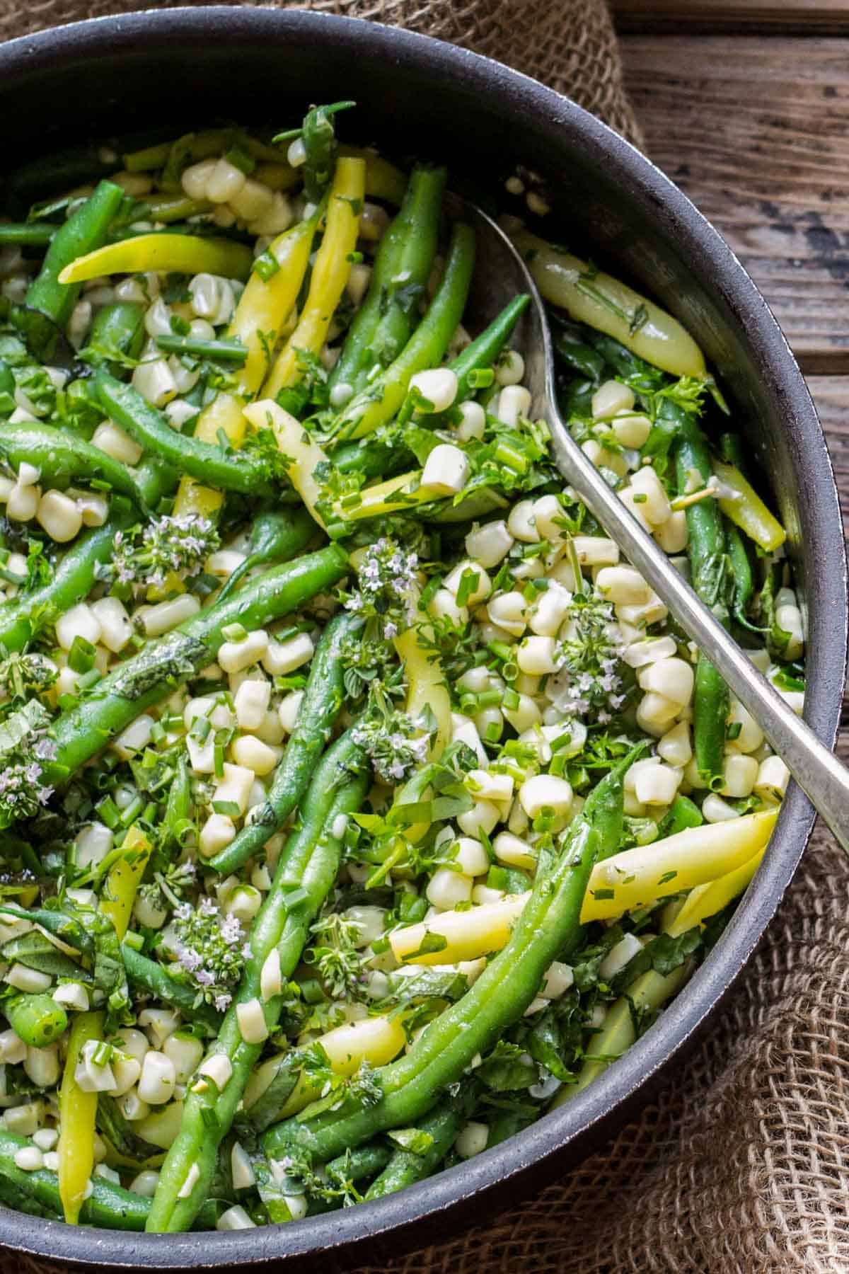 Green beans and corn in a pan with fresh herbs and a serving spoon. 