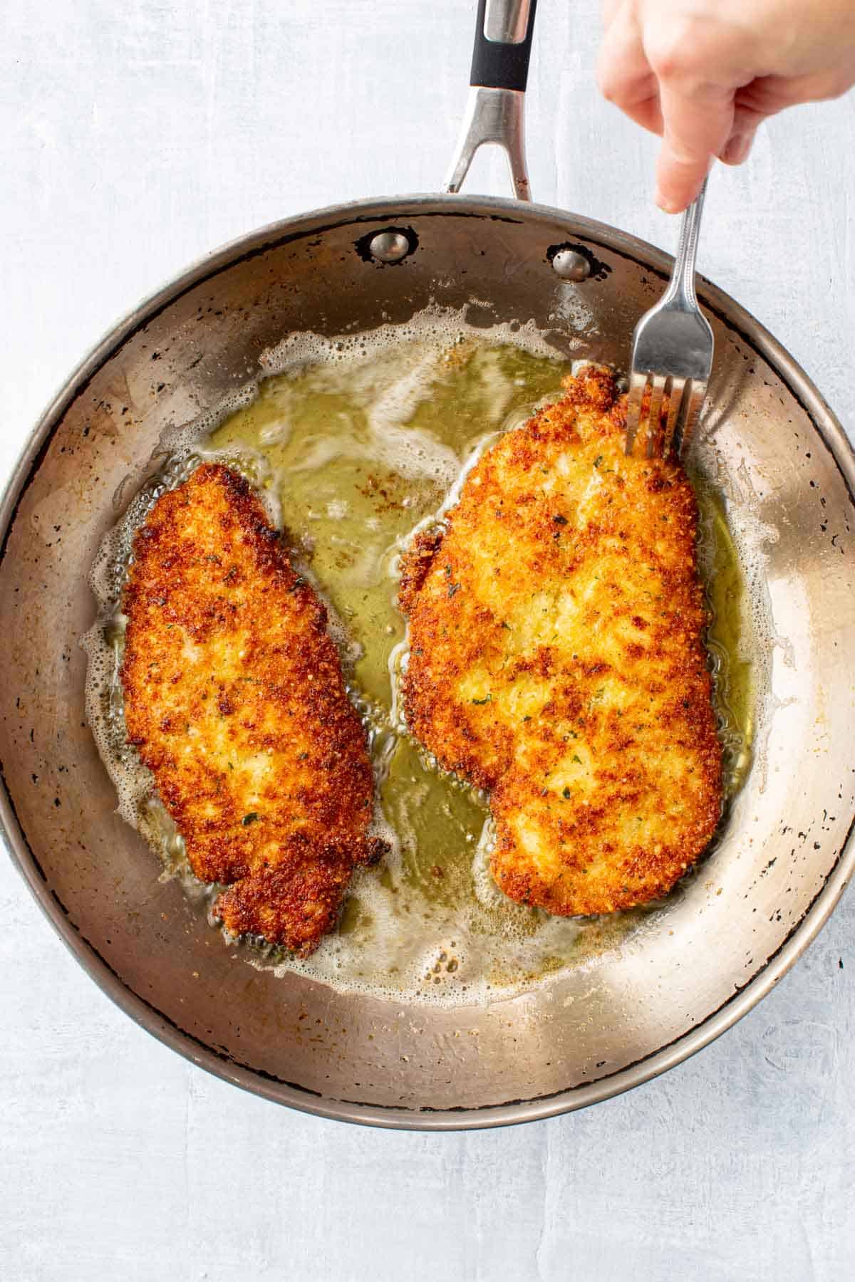 Pan frying two chicken cutlets in a pan with olive oil.