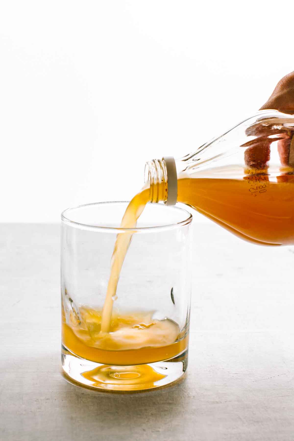 Pouring apple cider vinegar into a short clear glass.