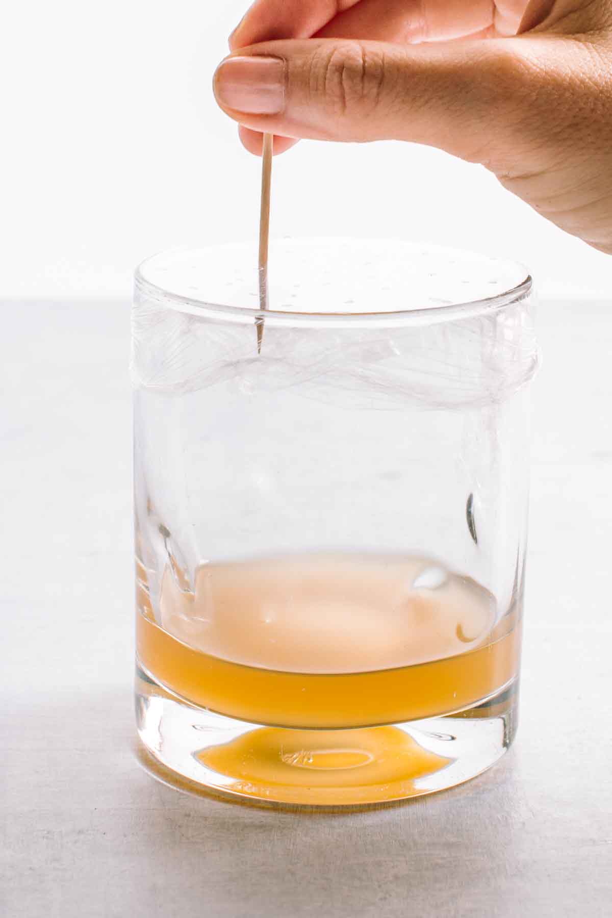 A toothpick poking holes in a glass filled with apple cider vinegar.