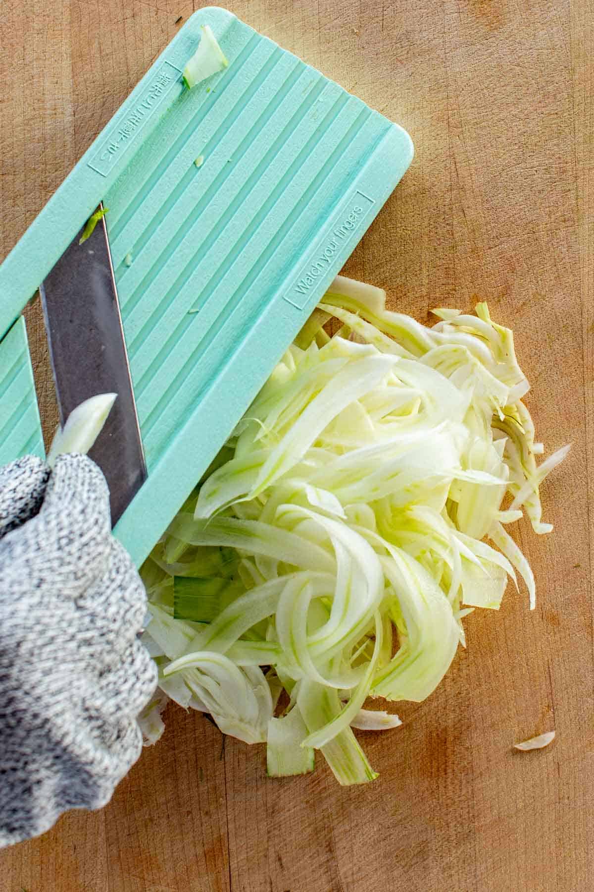 Shaving raw fennel on a mandoline slicer.