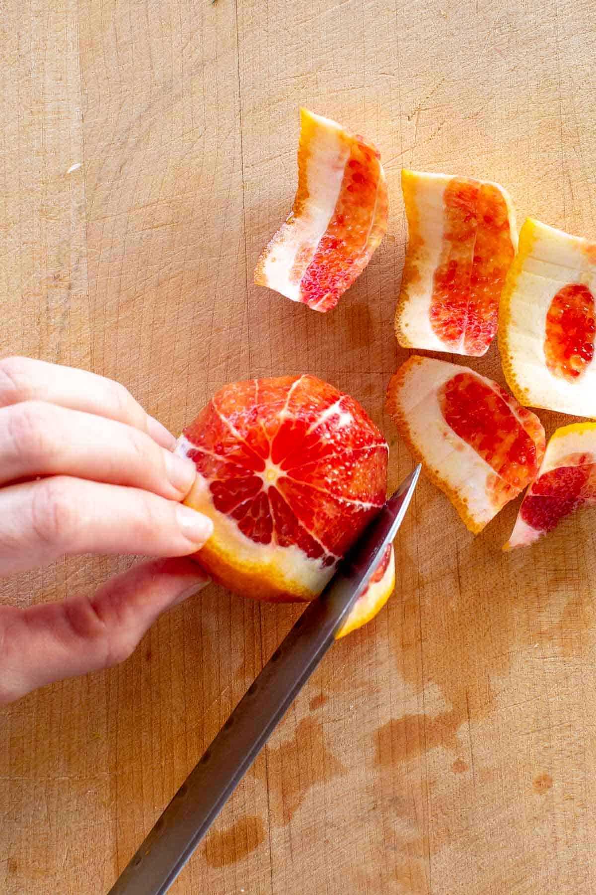 A knife removing the rind from a blood orange. 