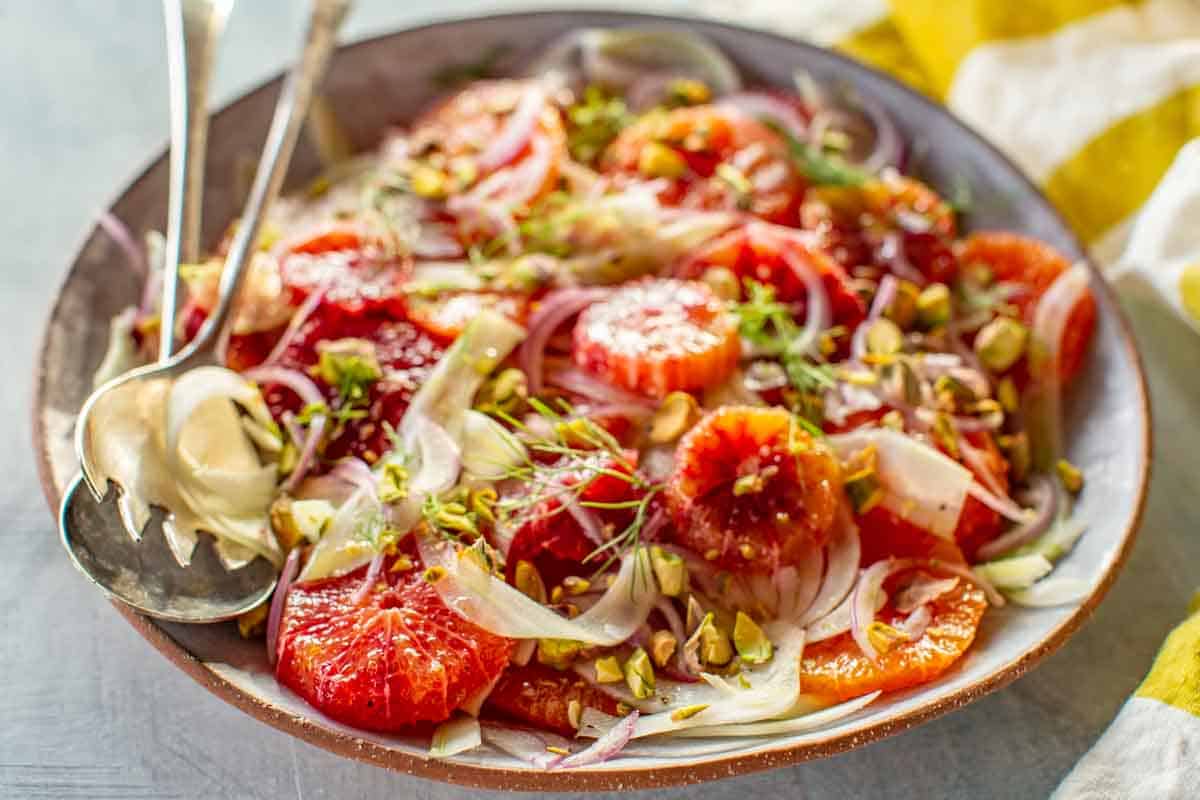 A platter of Sicilian blood orange and fennel salad with serving utensils.