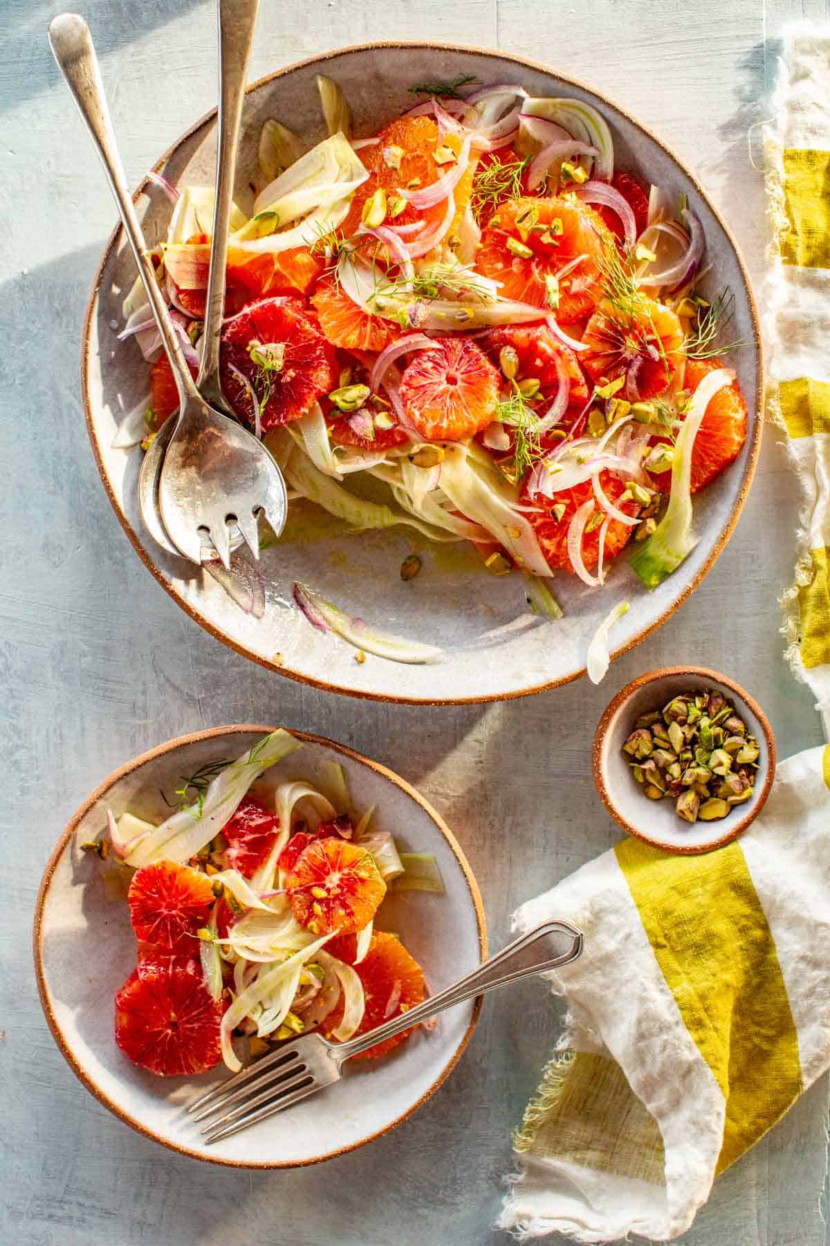 Two plates of fennel and orange salad with pistachios and silverware.