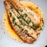 A fillet of white fish in a butter sauce garnished with parsley.