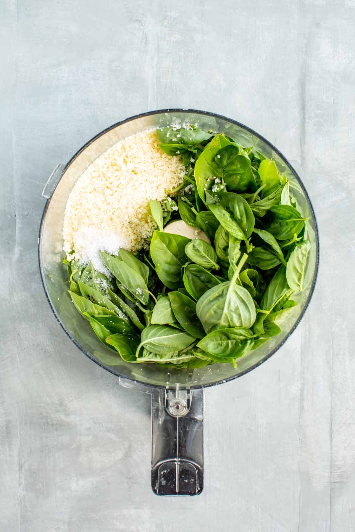 Fresh basil, garlic and cheese in the bowl of a food processor.