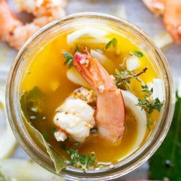 A piece of shrimp and herbs peeking out of a jar of pickle brine.