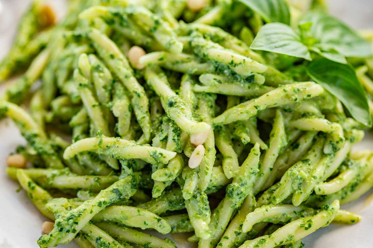 Close up of trofie pasta tossed with green basil pesto and pine nuts.