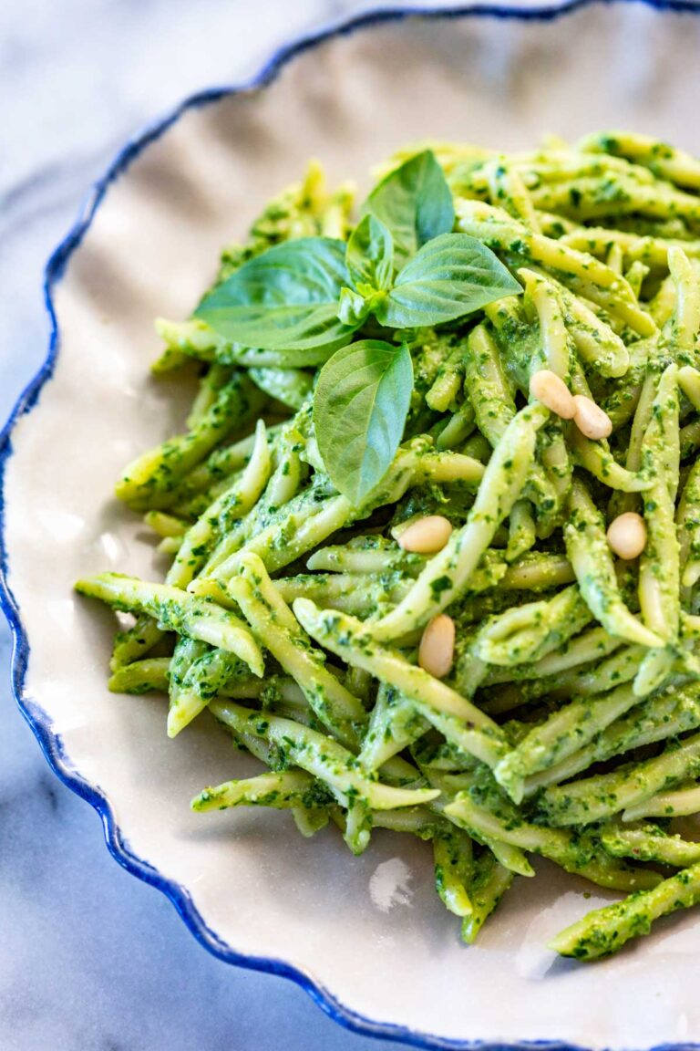 A plate of pesto pasta garnished with pine nuts and a sprig of basil.