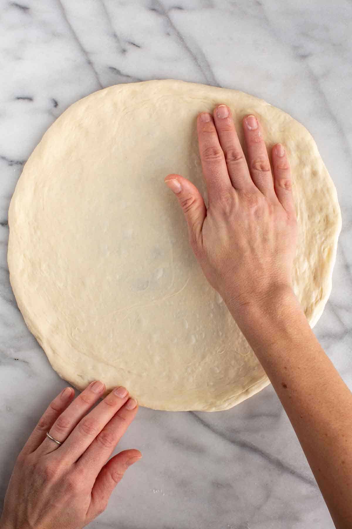 Hands stretching a piece of Neapolitan pizza dough into a circle.