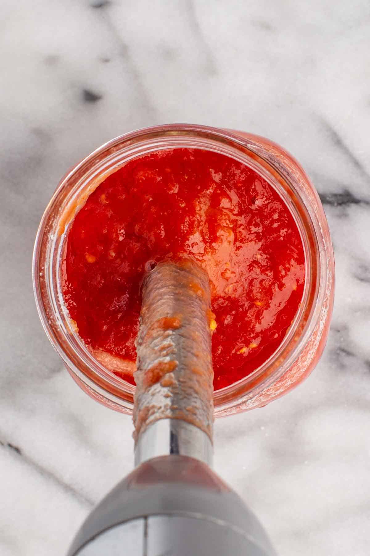 An immersion blender blending a jar of tomatoes.