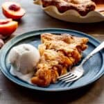 A blue plate with a slice of peach pie and a scoop of vanilla ice cream with a fork.