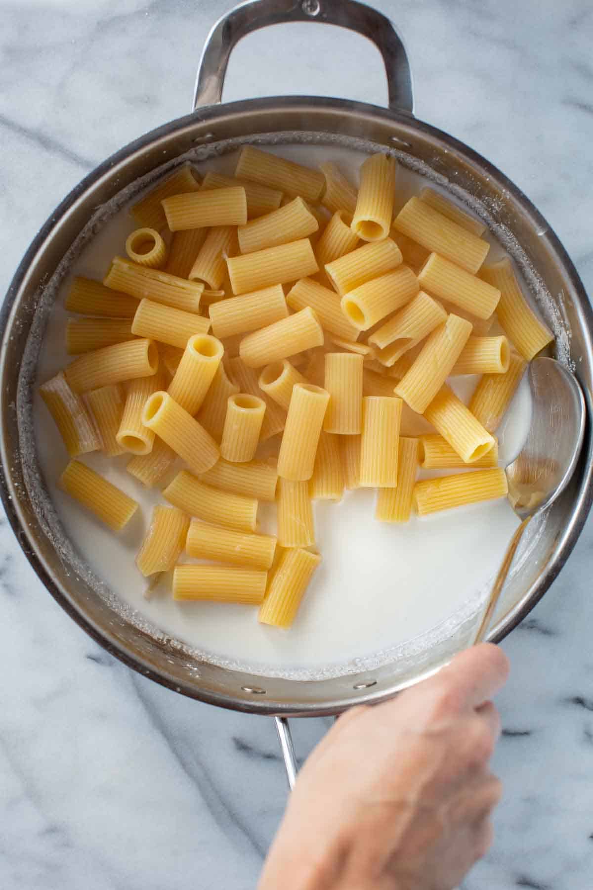 Rigatoni pasta being tossed in a pan with ricotta.