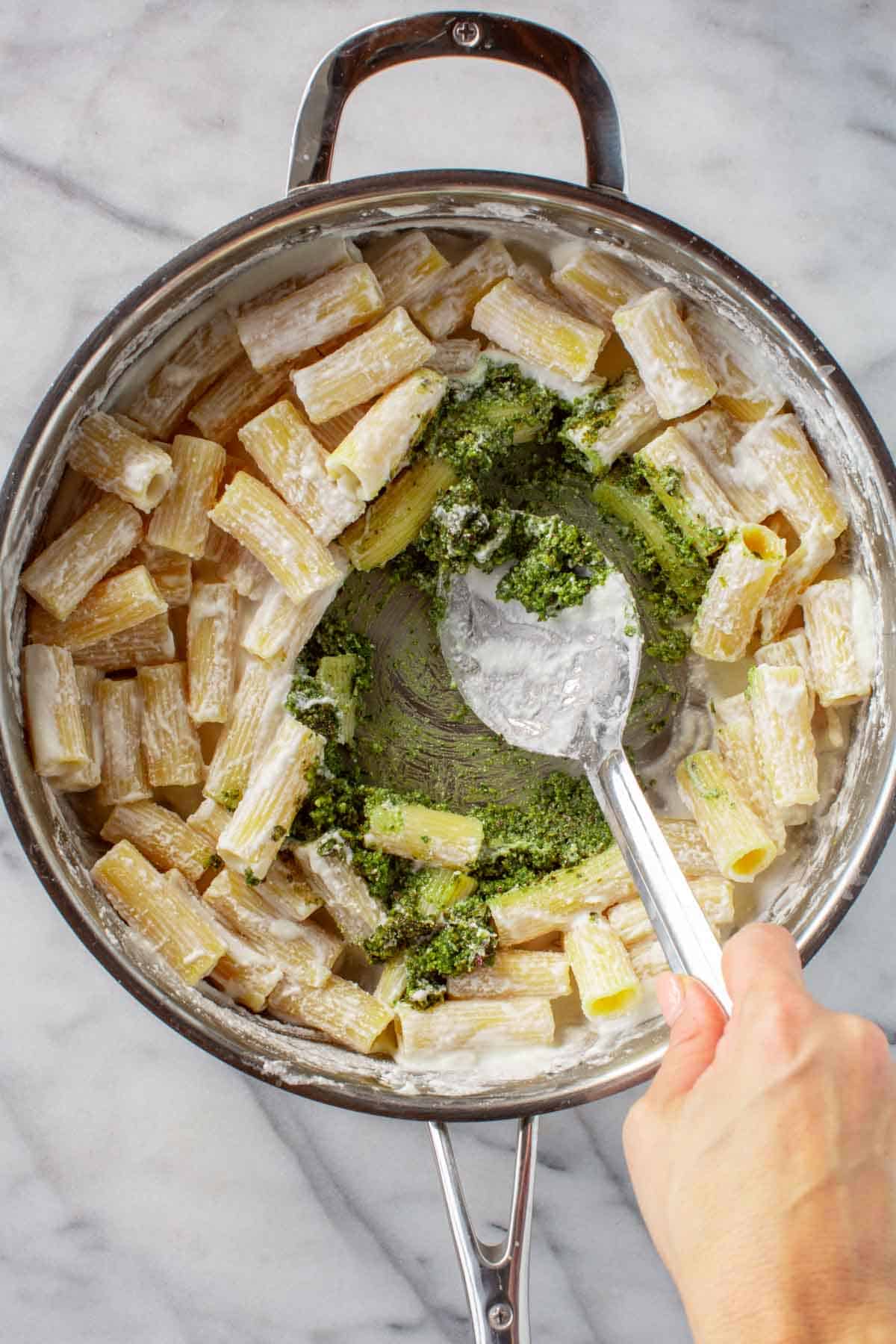 Mixing pesto into a pan of ricotta and rigatoni pasta.