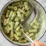 Scooping ricotta pesto pasta out of a pan.