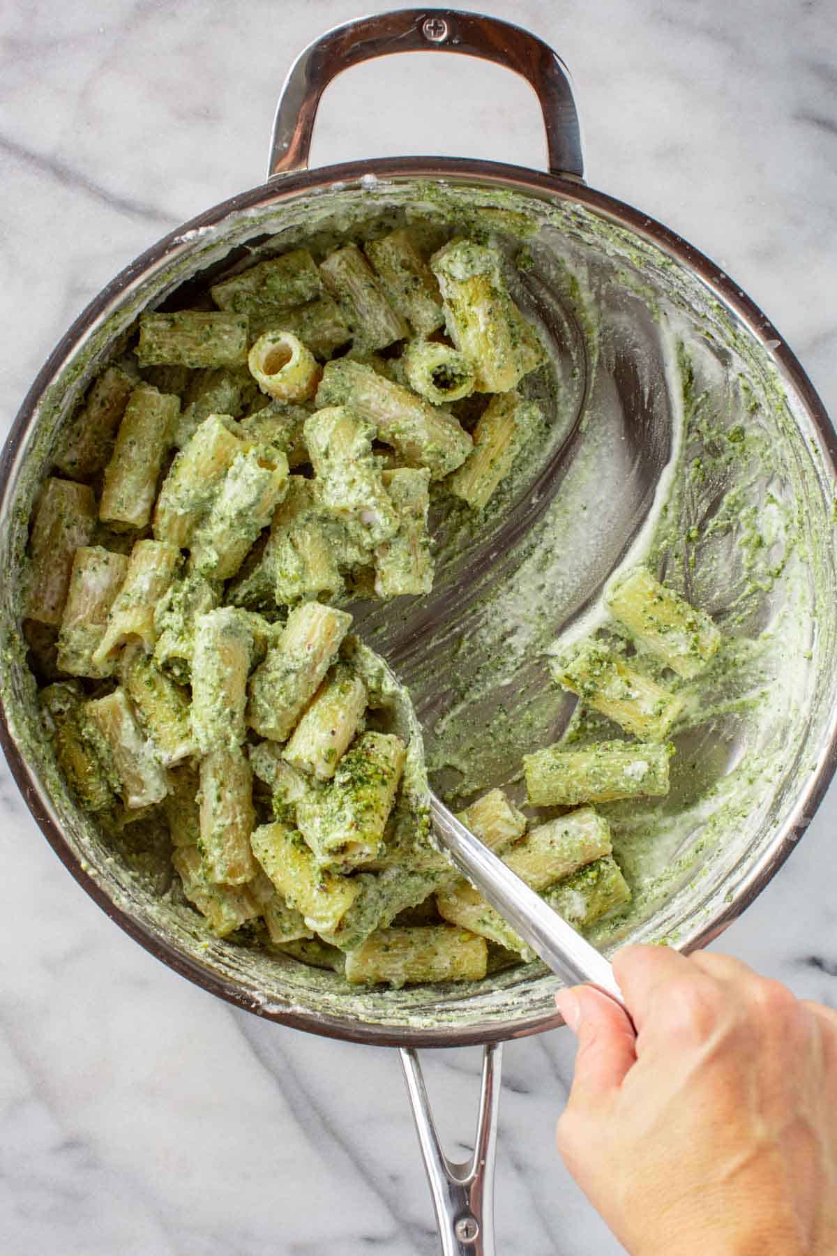 Scooping ricotta pesto pasta out of a pan.