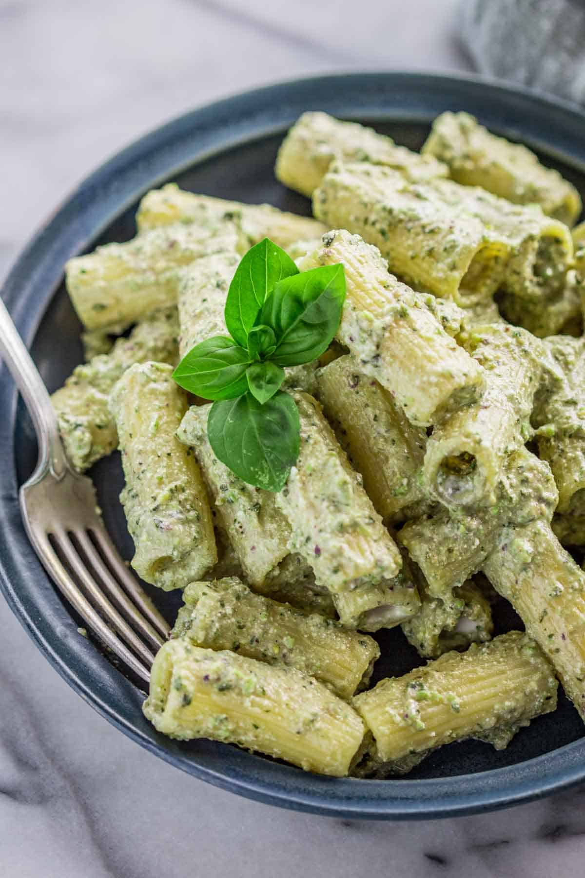 A plate of ricotta pesto pasta with a basil sprig and fork. 