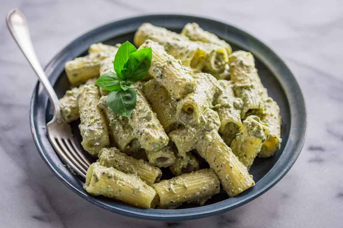 A blue plate with rigatoni tossed with ricotta and pesto.