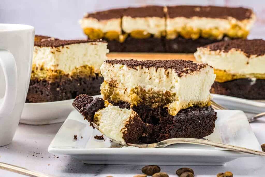 A few slices of tiramisu brownies on plates, one has a bite taken out with a fork.