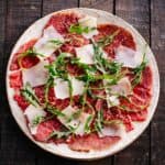 A plate of carpaccio of beef on a wooden table.